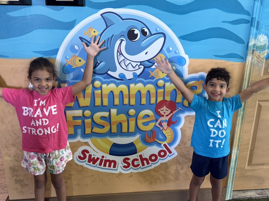 Two young swimmers posing by the Swimming Fishies logo